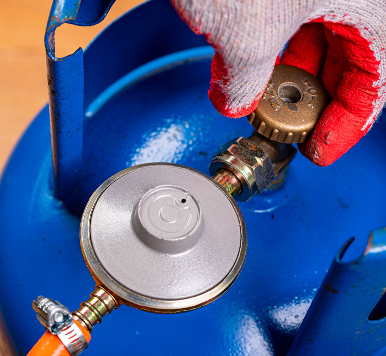Mano con guanti da lavoro rossi che avvita il regolatore di pressione su una bombola GPL blu per il riscaldamento