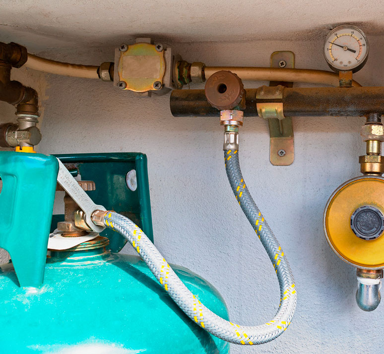 Primo piano su bombola del gas verde collegata a tubi di rame e manometro a muro.