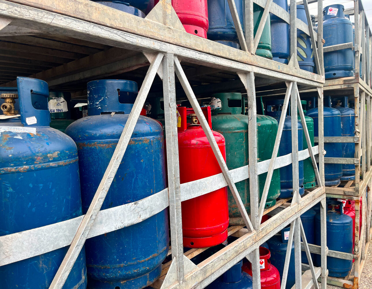 Bombole GPL industriali blu, rosse e verdi stoccate su rastrelliere metalliche.
