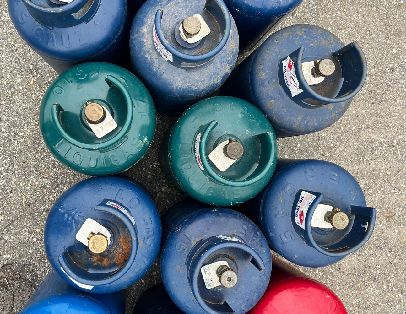 Inquadratura dall'alto di diverse bombole GPL industriali blu e verdi, con valvole.